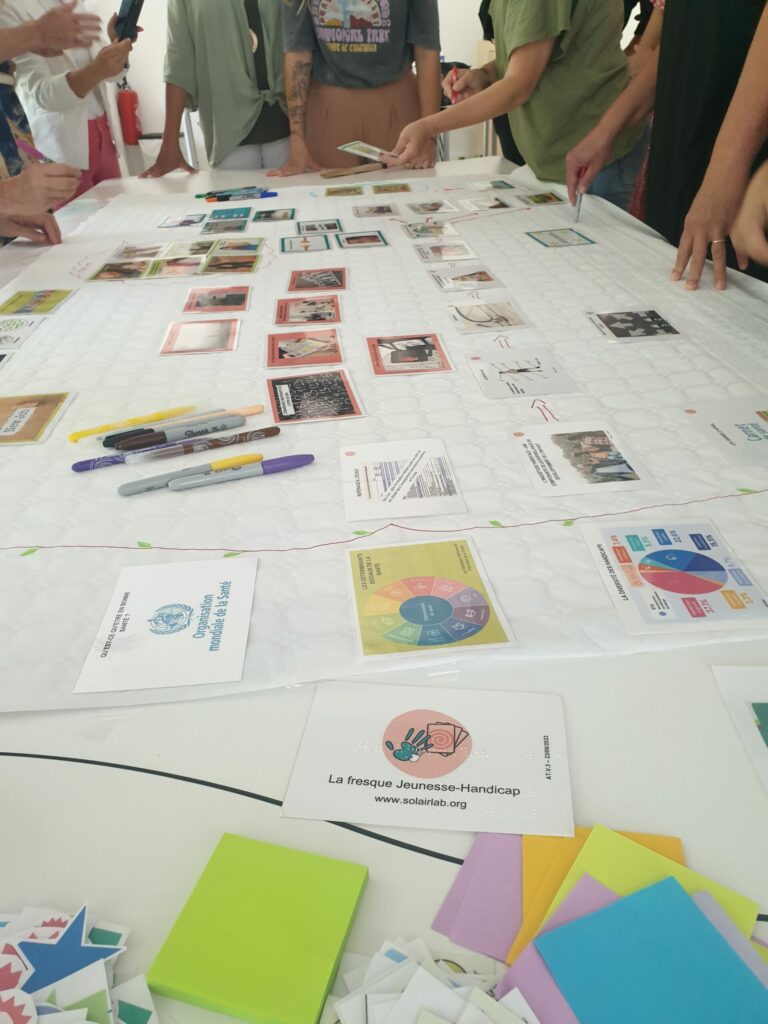 photo de cartes colorées et avec du texte sur une table, il y a des gens debout autour.