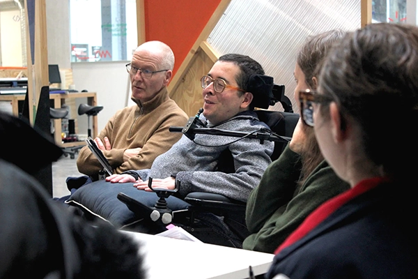 4 personnes assises regardent une présentation, l'une d'elle est en fauteuil roulant