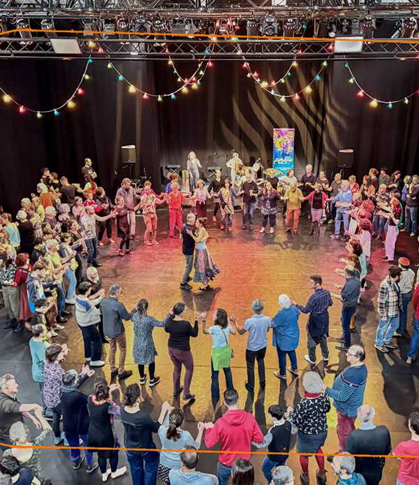 photo d'un bal inclusif où on voit un homme et une femme danser au milieu d'un cercle de personnes qui se tiennent la main dans une foule